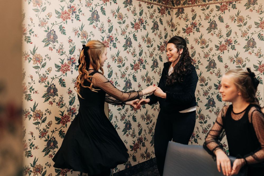 Women in black dresses dancing together against floral wallpaper.