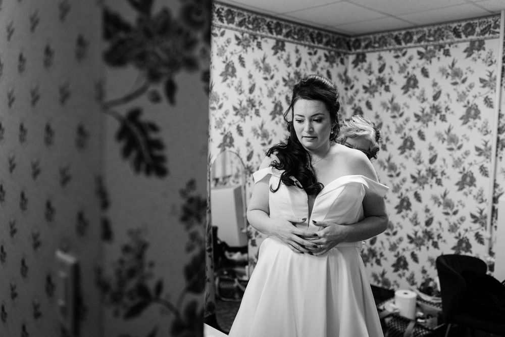 Black and white photo of a bride in an elegant off-shoulder wedding dress getting ready.