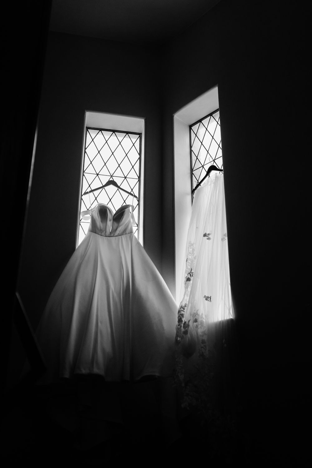 Series of dark silhouettes showing a white wedding dress hanging in a window with diamond panes.