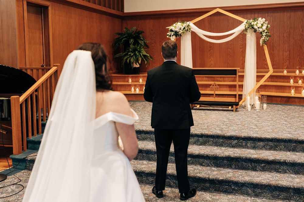 A couple standing before a floral wedding arch in a ceremony space.