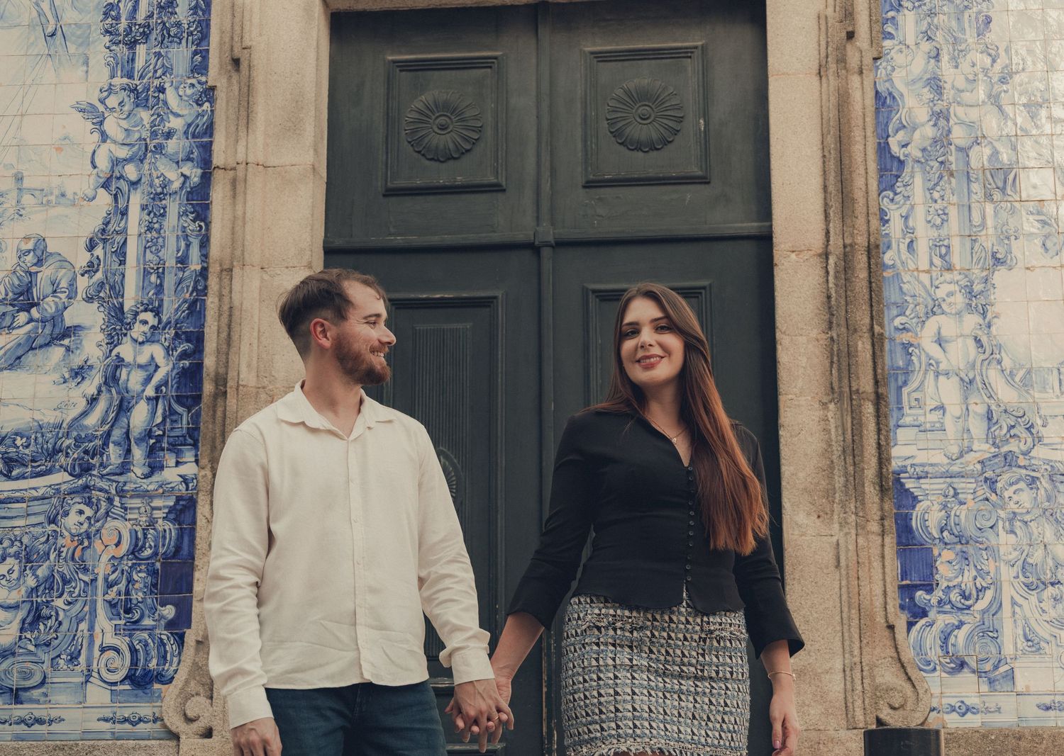 Couple walking past traditional blue and white tile artwork on building exterior.