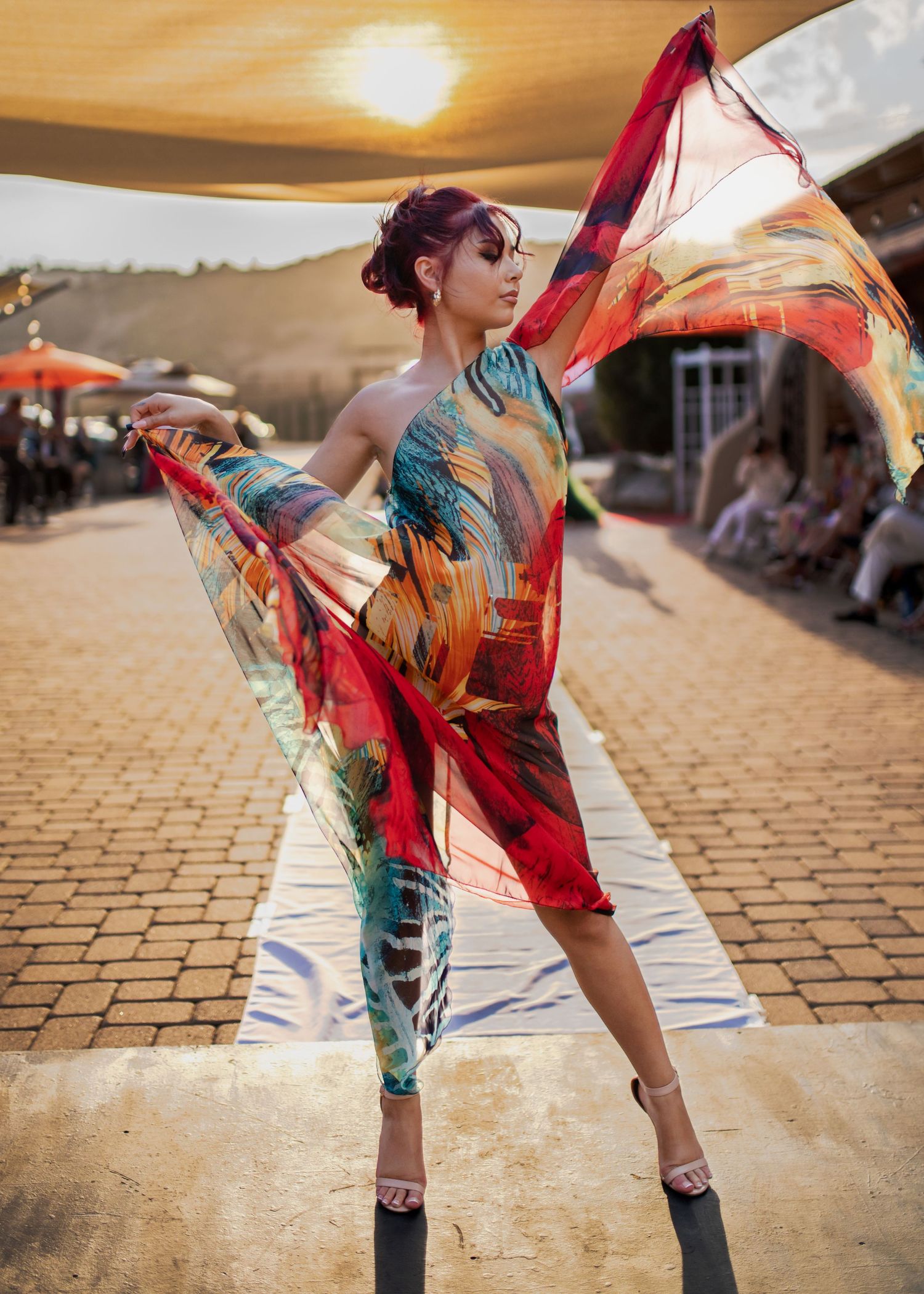 Dancer in colorful flowing dress performs at sunset on cobblestone street.