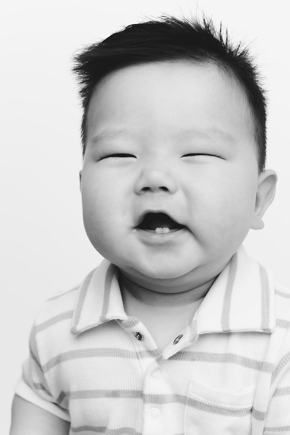 Black and white portrait of a happy child in striped polo shirt with eyes in cheerful crescents.