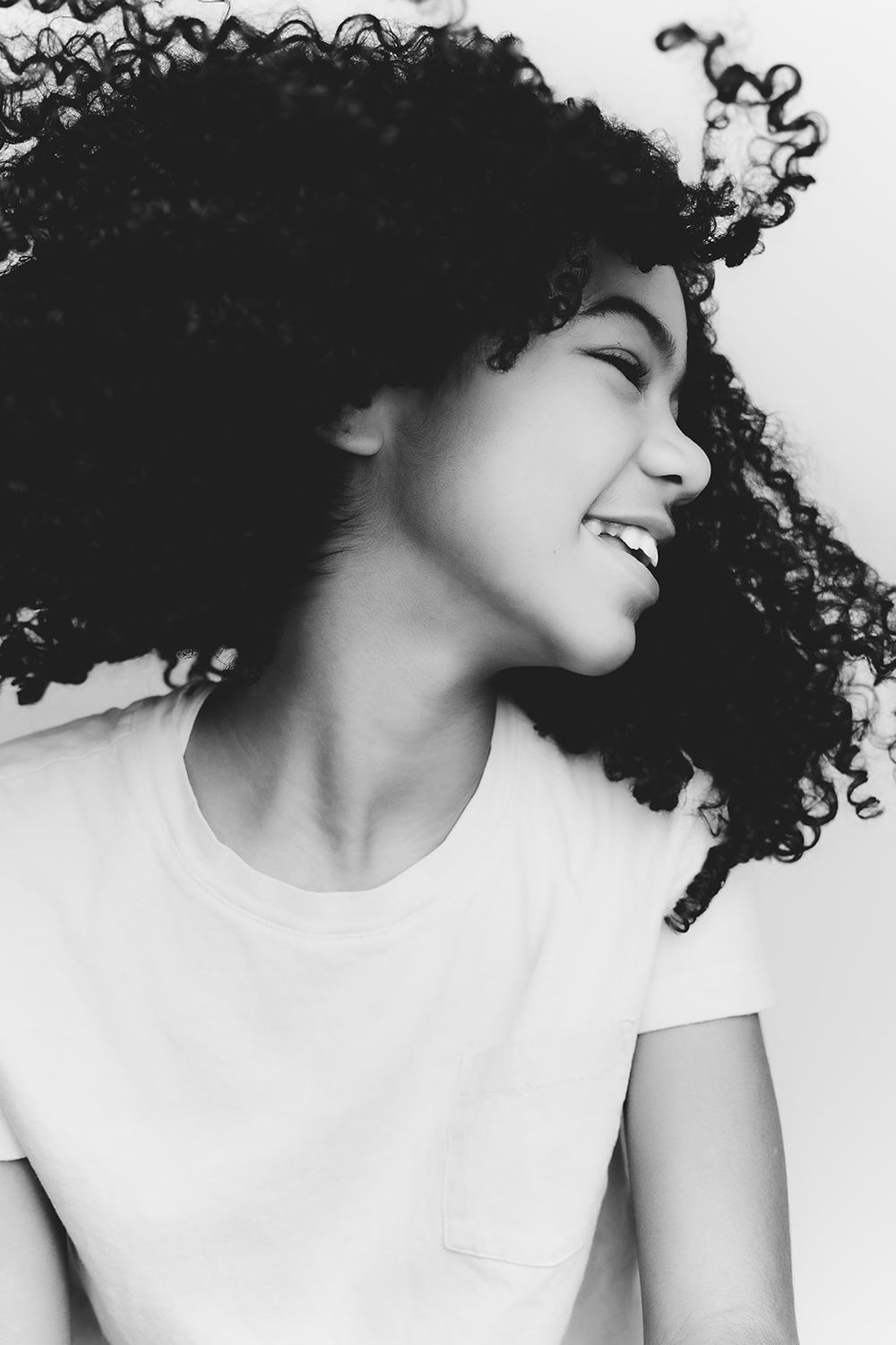 Black and white portrait of a person with curly hair laughing joyfully in profile.