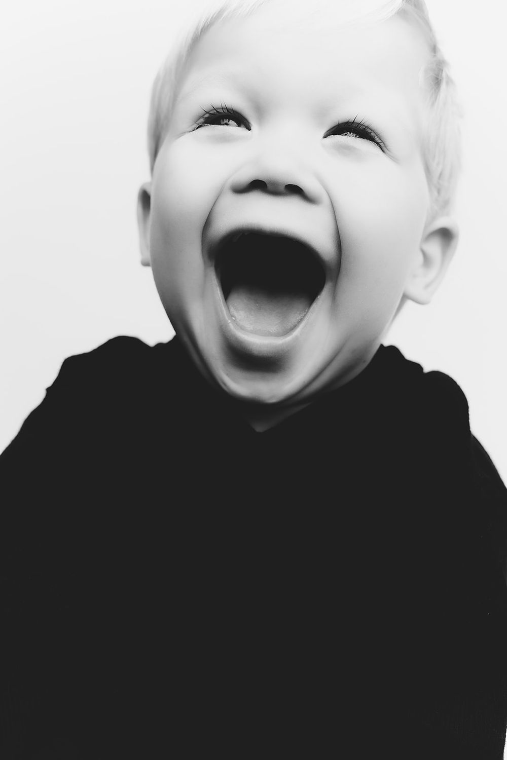 Black and white close-up of a child with wide open mouth expressing pure joy.