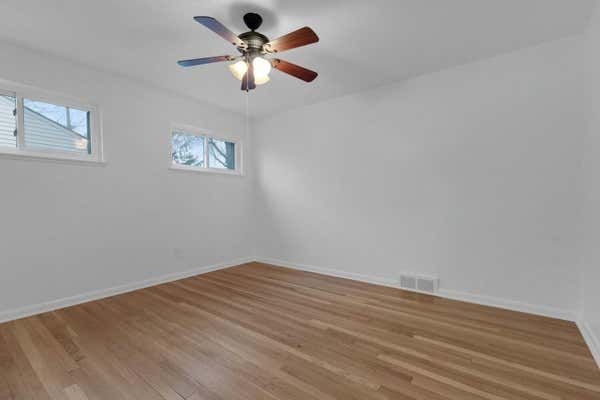 Sunlit empty bedroom with hardwood floors, ceiling fan, and white walls.