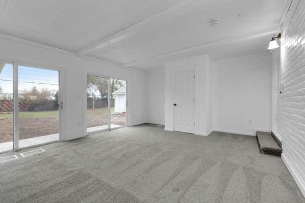 Bright enclosed sunroom with gray carpet, sliding glass doors, and white brick walls.