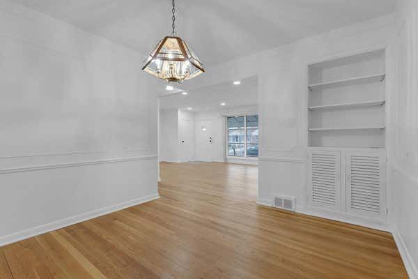 Elegant dining room with hardwood floors, chandelier, built-in shelves, and louvered doors.