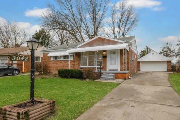 Brick ranch home at 3042 with covered porch, attached garage, green lawn, and mature trees in a suburban neighborhood.