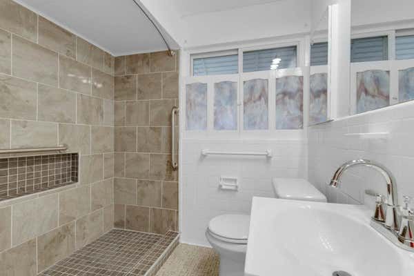 Clean bathroom with tiled walk-in shower, niche shelf, toilet, pedestal sink, and frosted glass window.