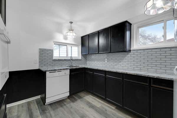 Modern kitchen with dark cabinets, gray subway tile backsplash, granite countertops, and white dishwasher.