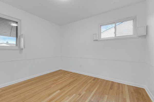 Small empty bedroom with light hardwood floors, white walls, and two windows providing natural light.