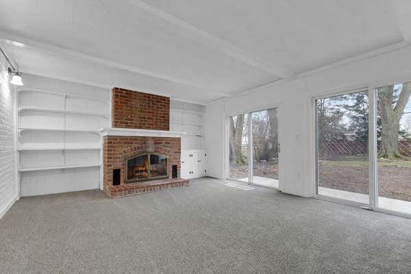Sunroom with brick fireplace, built-in shelves, gray carpet, and sliding glass doors overlooking backyard.