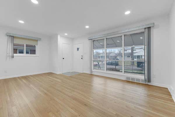 Bright living room with light hardwood floors, recessed lighting, large window, and white walls.