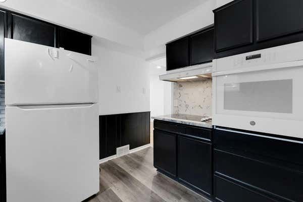 Modern kitchen with black cabinets, white appliances, marble backsplash, and hardwood floors.