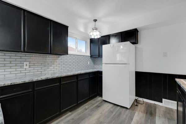 Kitchen with dark cabinets, subway tile backsplash, white refrigerator, and hardwood floors.
