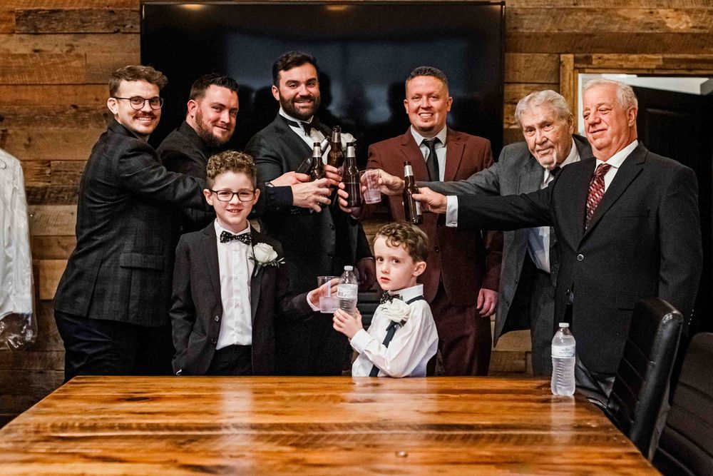 Group toasting with drinks at a celebration in rustic wooden venue. Groom and groomsmen getting ready.