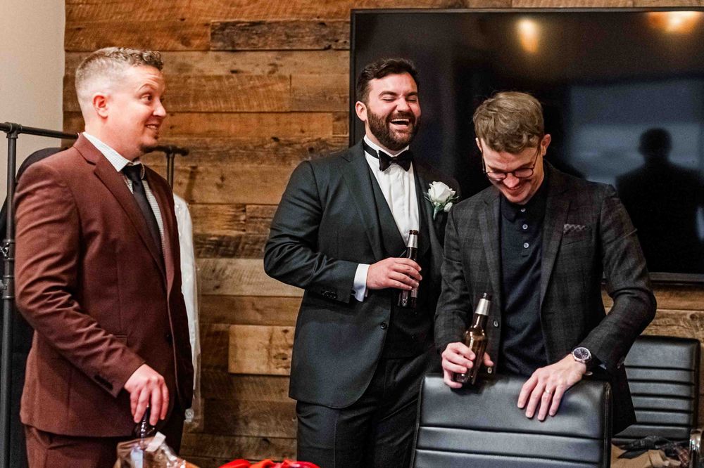 Three men in formal attire laughing and enjoying drinks together.
