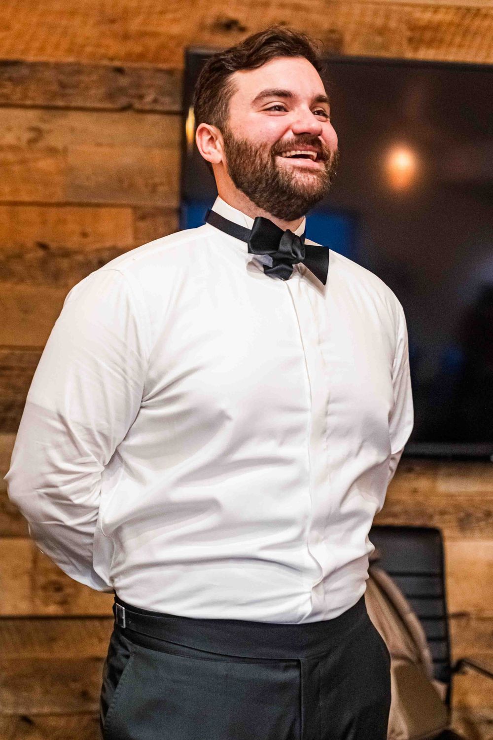 Formal portrait of man in white shirt and bow tie against wooden wall. Groom portrait.