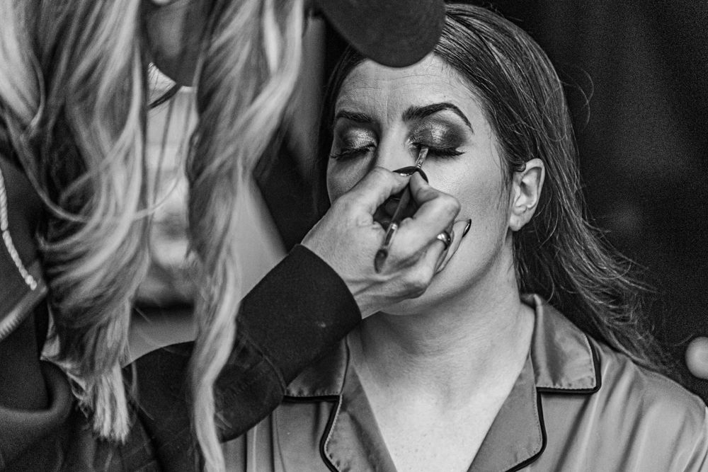 Black and white image of bride getting eye makeup done by a professional makeup artist