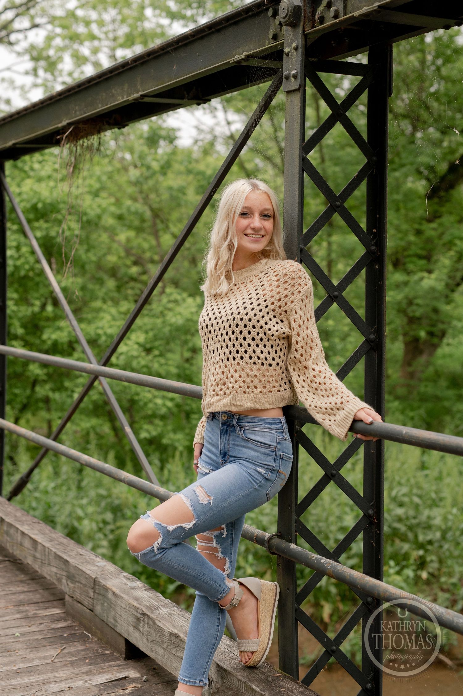 Fashion portrait on wooden bridge wearing distressed jeans and crochet sweater.
