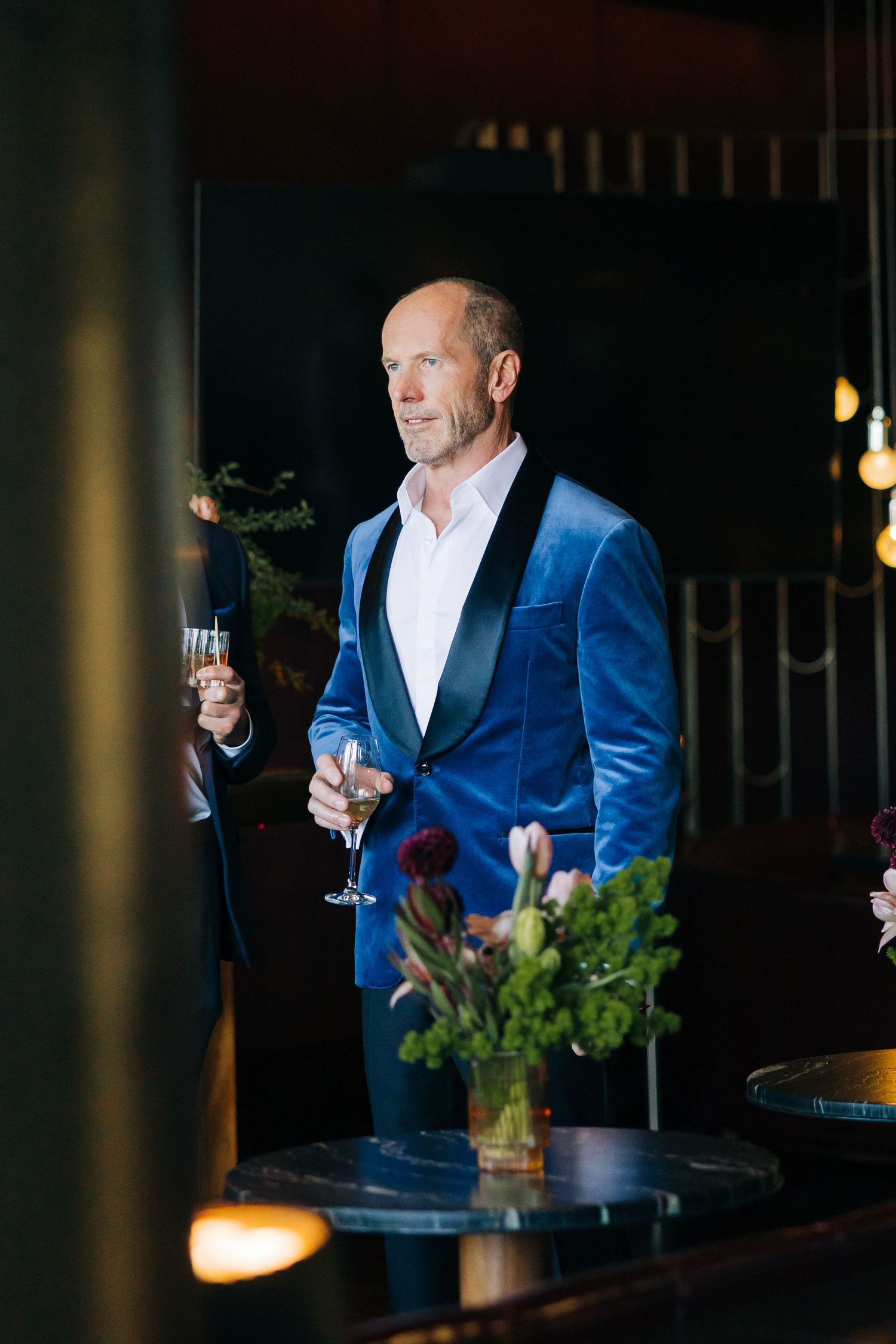 A person in a blue velvet blazer holds a champagne glass at an elegant evening event.