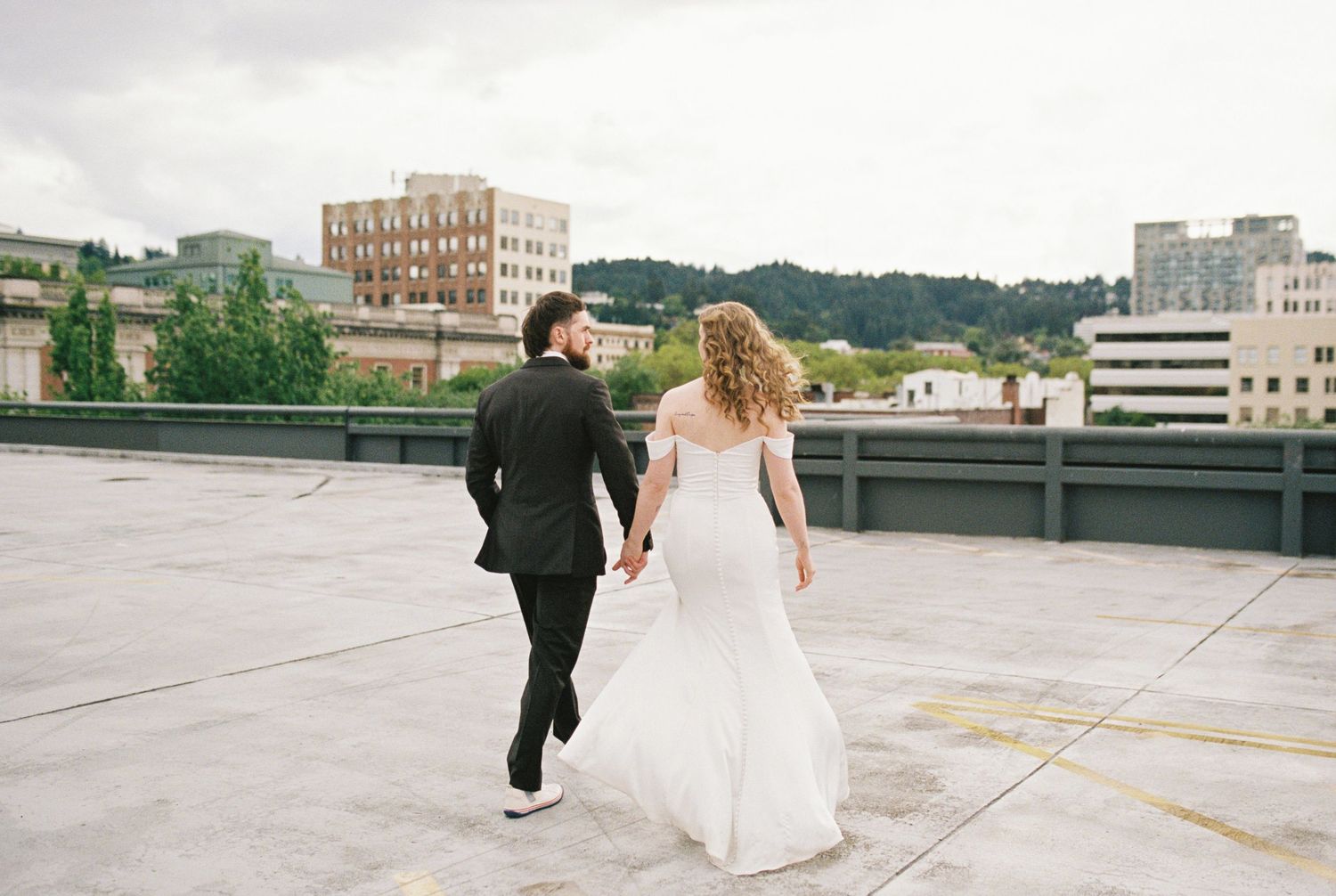 Two people embrace on a white columned porch overlooking a scenic grassy lawn with evergreen trees in the distance.