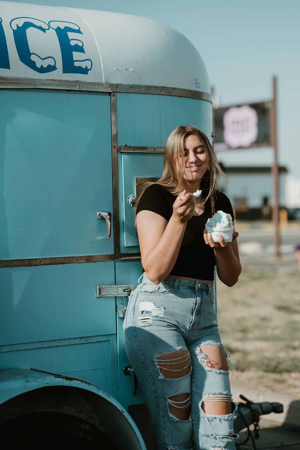 Playful poses next to a vintage blue ice truck wearing ripped jeans and black top.