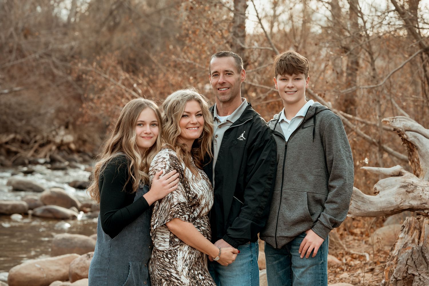 Family group poses together on fallen logs in an autumn woodland setting.