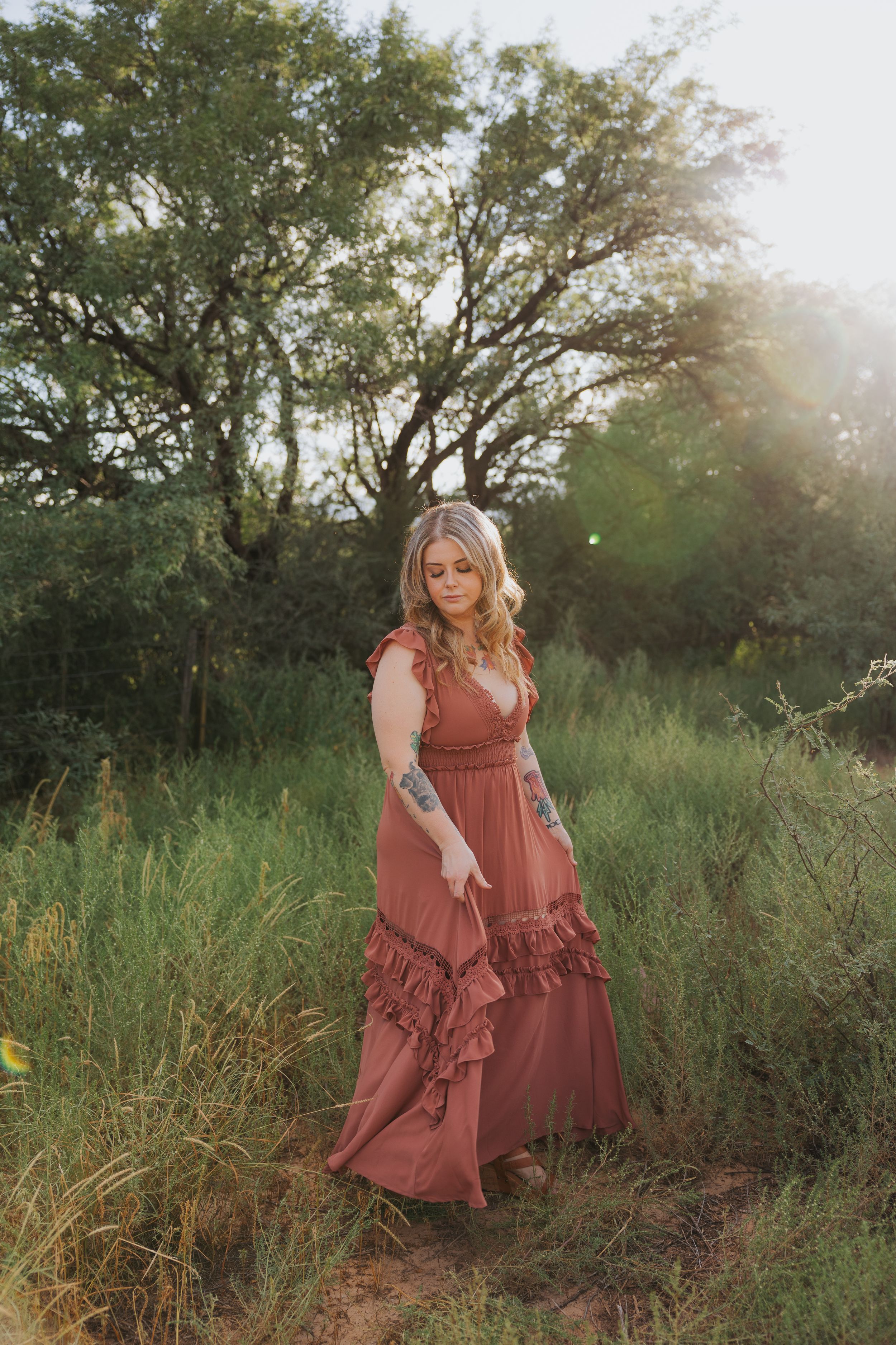 A rustic outdoor portrait featuring a flowing rust-colored maxi dress with tiered ruffles.