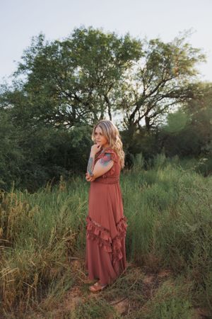 A bohemian style photoshoot featuring a rust-colored maxi dress in a wild grass setting.