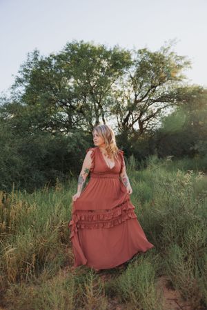 A dreamy outdoor fashion photo featuring a flowing rust-colored dress among tall grass.
