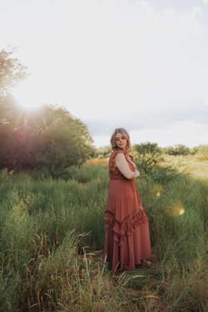 A romantic sunset photoshoot featuring a rust-colored maxi dress in a natural setting.