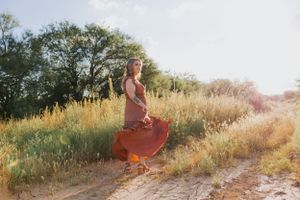 Woman twirls in rustic dress among tall grass during golden hour photography session.