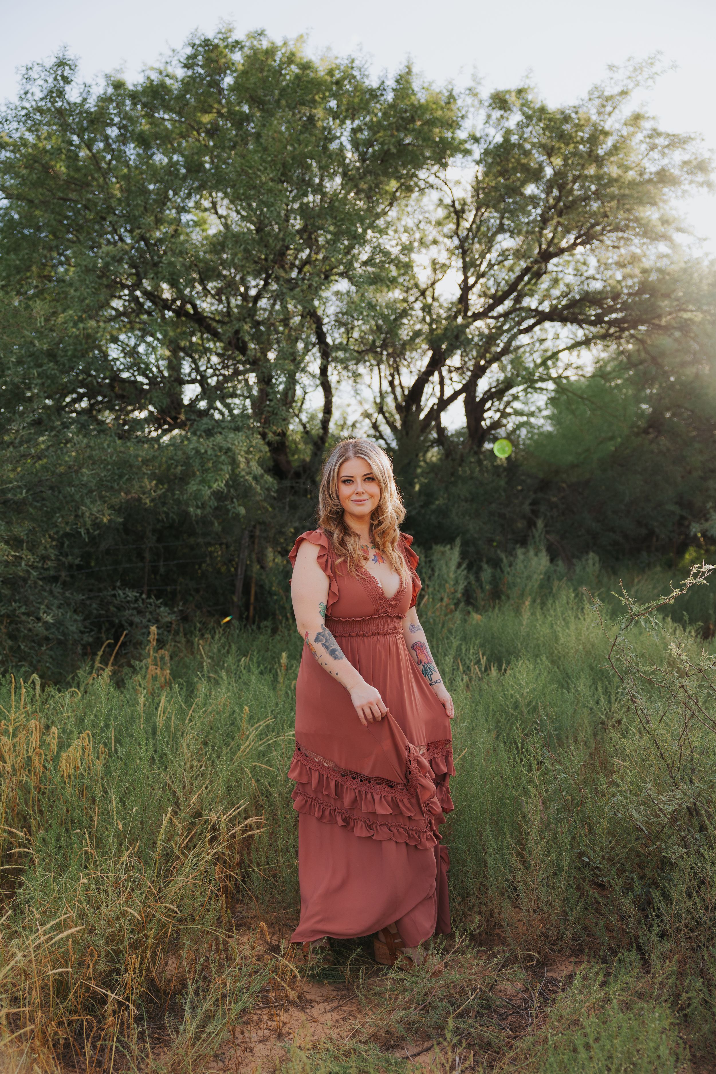 A romantic outdoor scene with a flowing rust-colored dress against a backdrop of trees and wild grass.