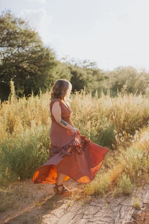 Dancing figure in rust-colored dress moves gracefully through sunlit field.