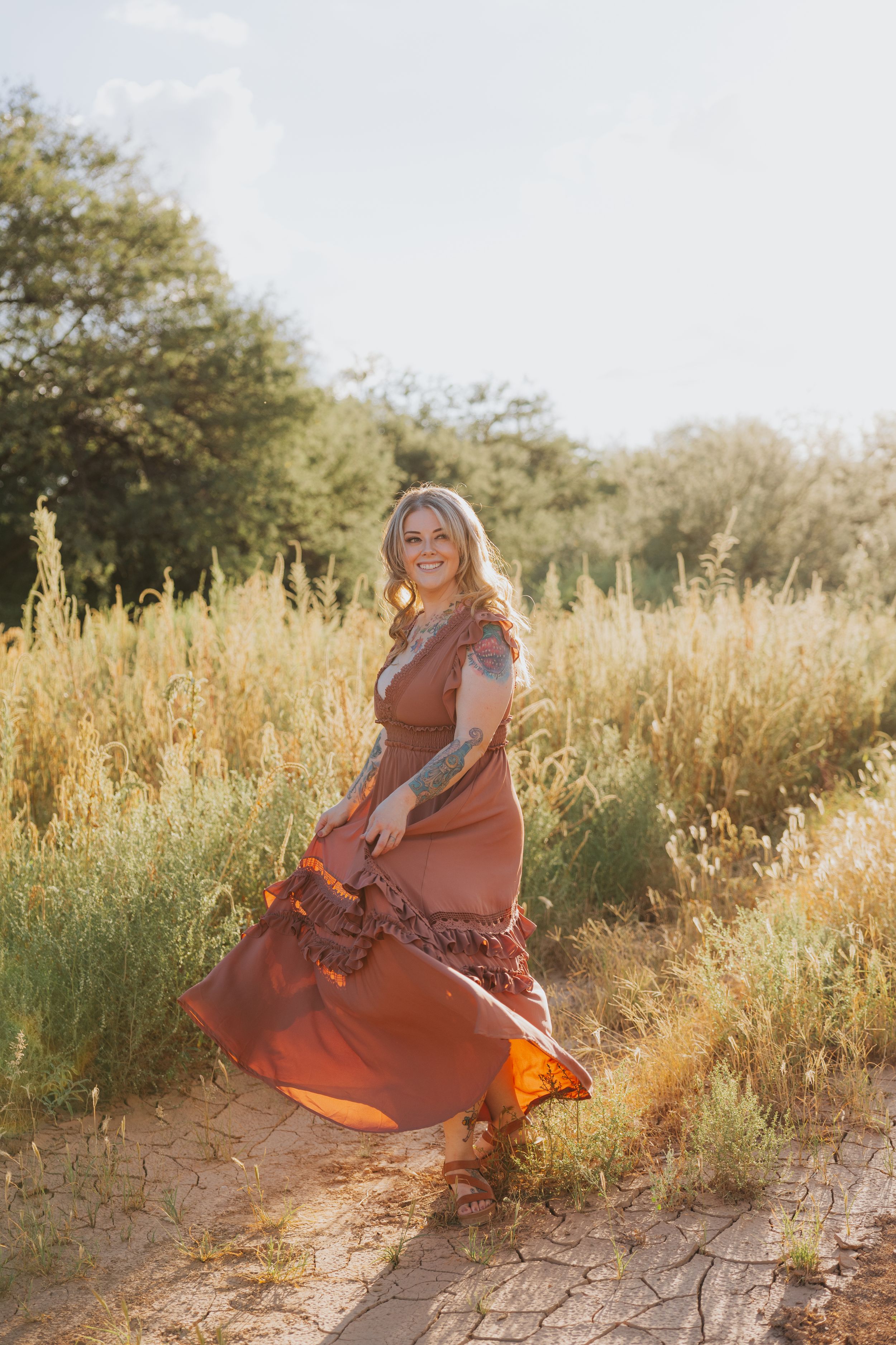 Woman in flowing dress spins through golden grass during sunset photoshoot.