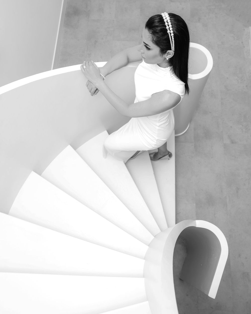 Artistic black and white photograph of bride descending modern spiral staircase.