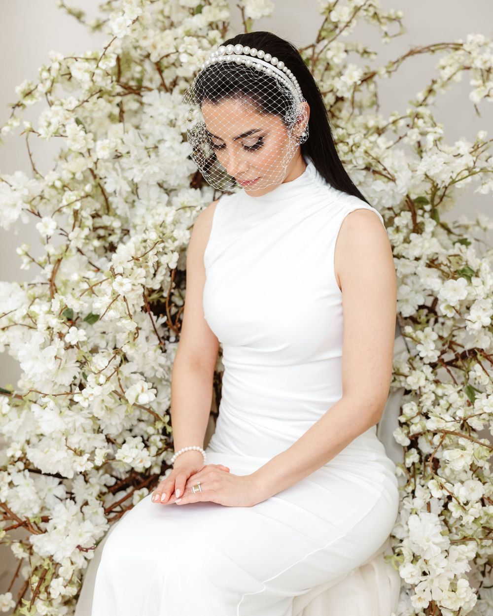 Elegant bridal portrait with vintage veil headpiece against white floral installation backdrop.