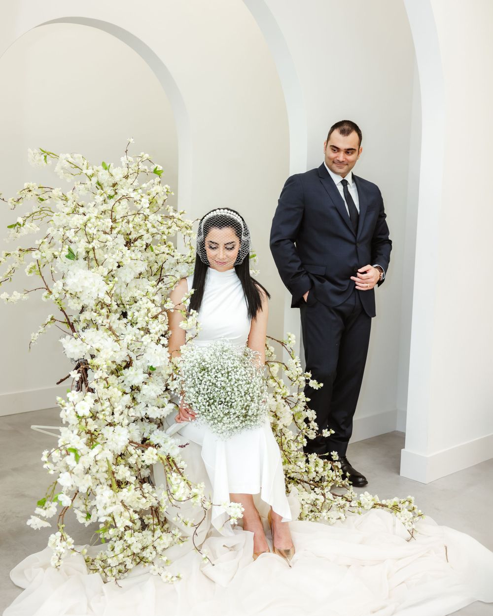 Modern wedding scene with couple posing in white archway surrounded by elegant floral arrangements.