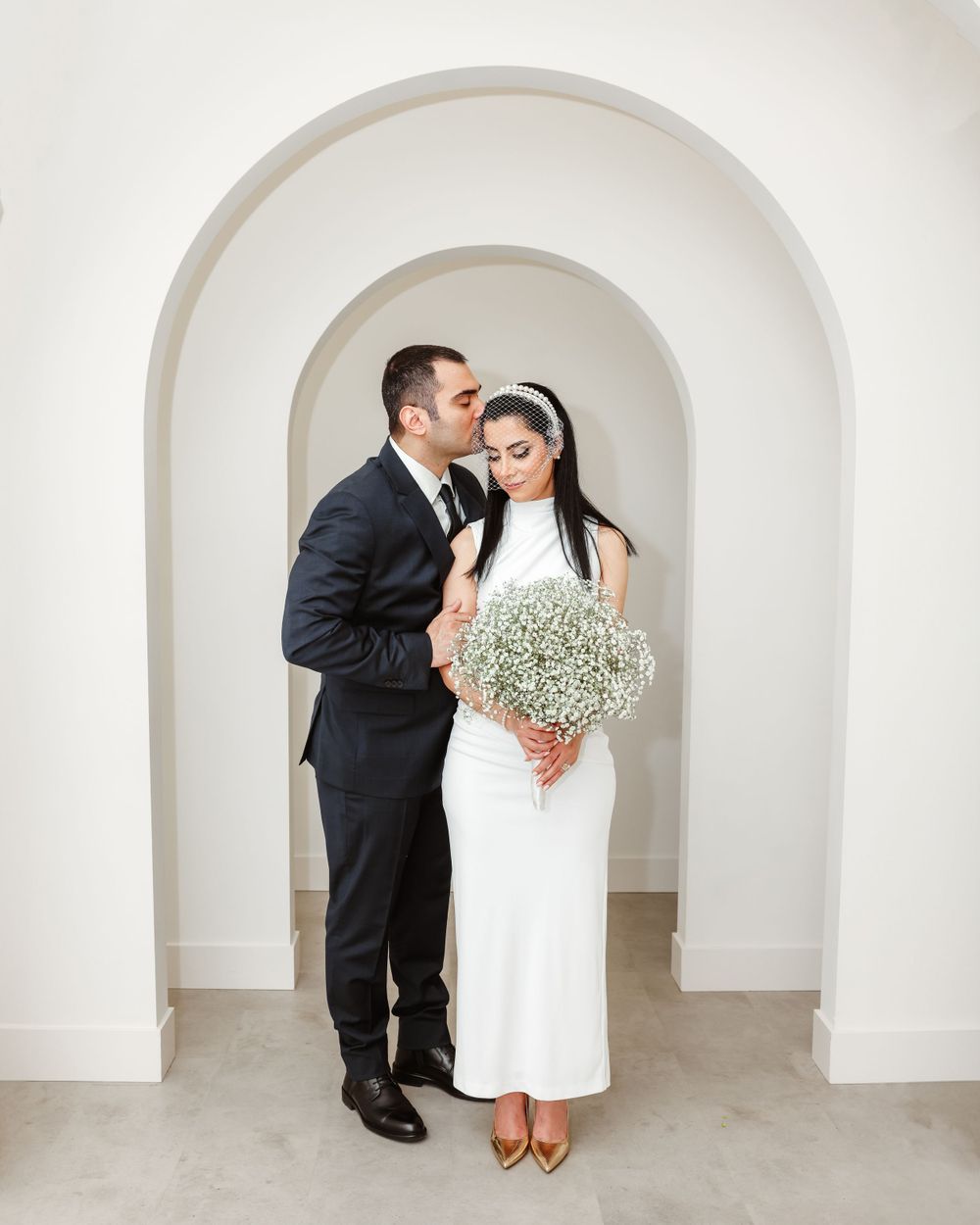 Intimate wedding portrait under white archway with baby's breath bouquet.