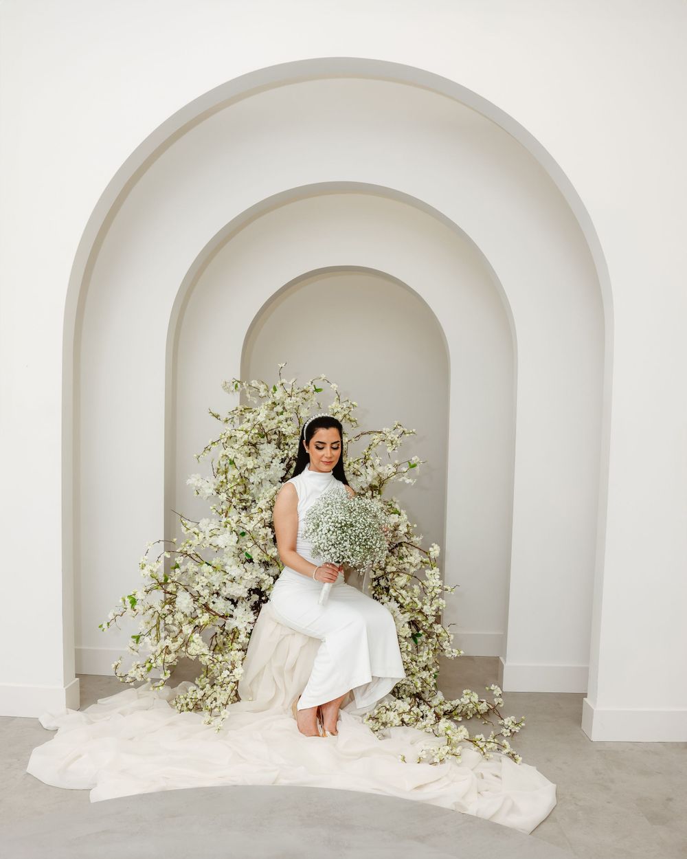 Bride poses in arched doorway decorated with white baby's breath flowers.