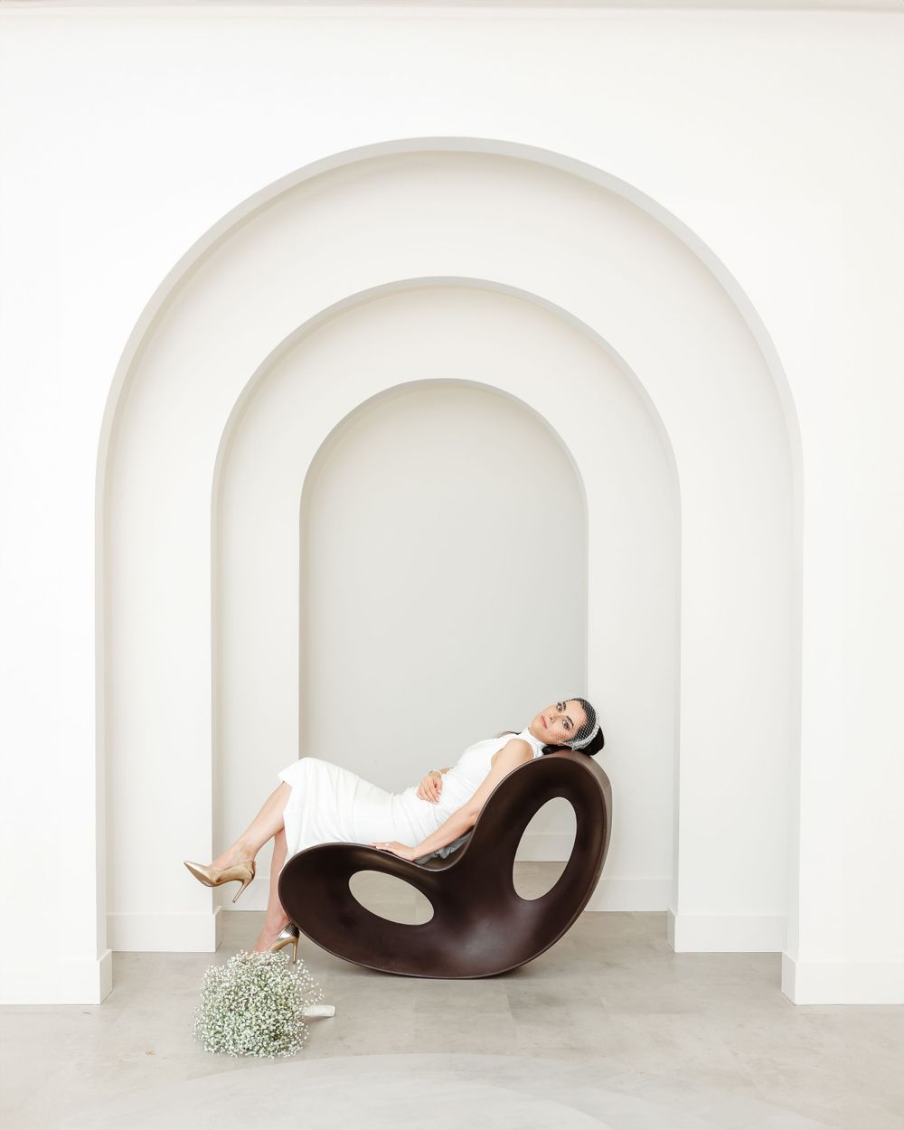 Modern bridal portrait with sculptural chair in white arched gallery space.