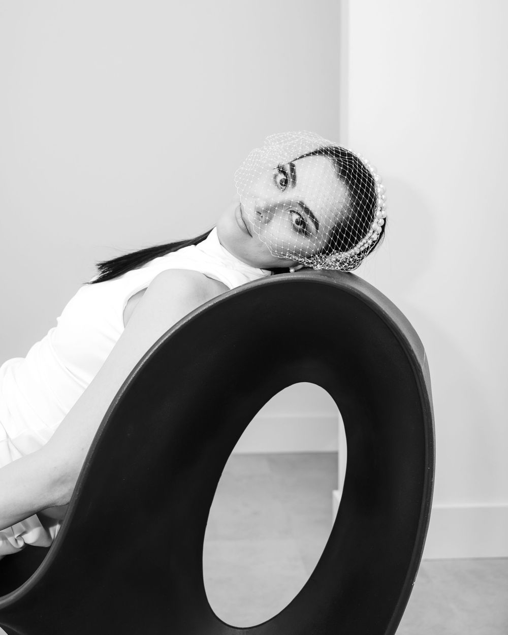 Black and white portrait on modern sculptural chair with architectural background.