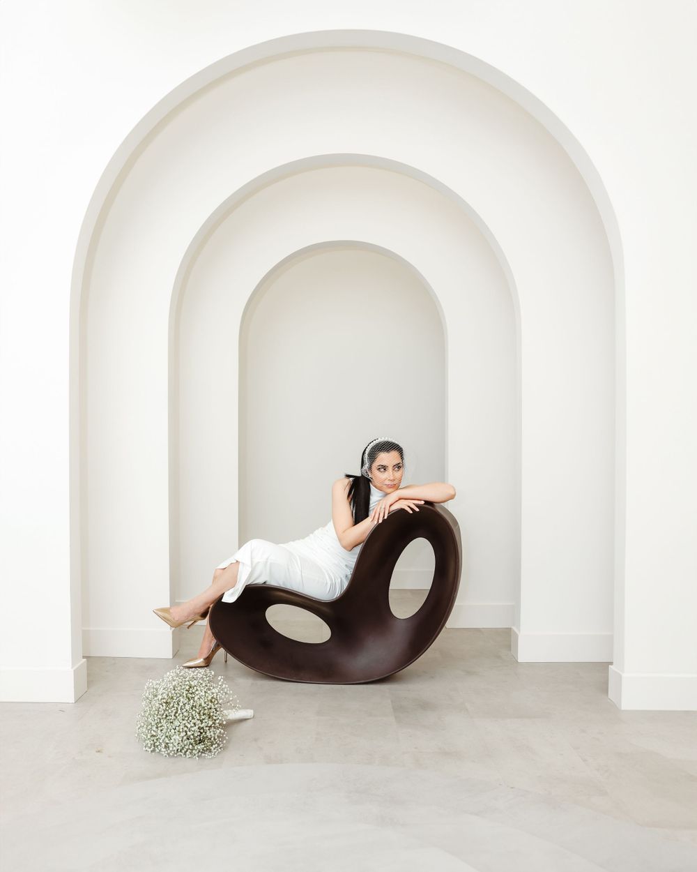 Wedding photo in minimalist white archway with modern curved lounge chair and delicate floral arrangement.