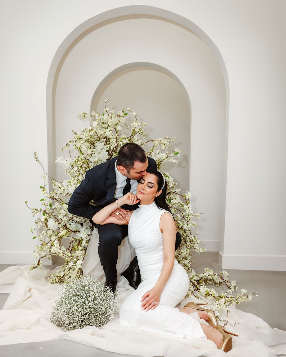Romantic wedding moment captured in white archway adorned with delicate baby's breath flowers.