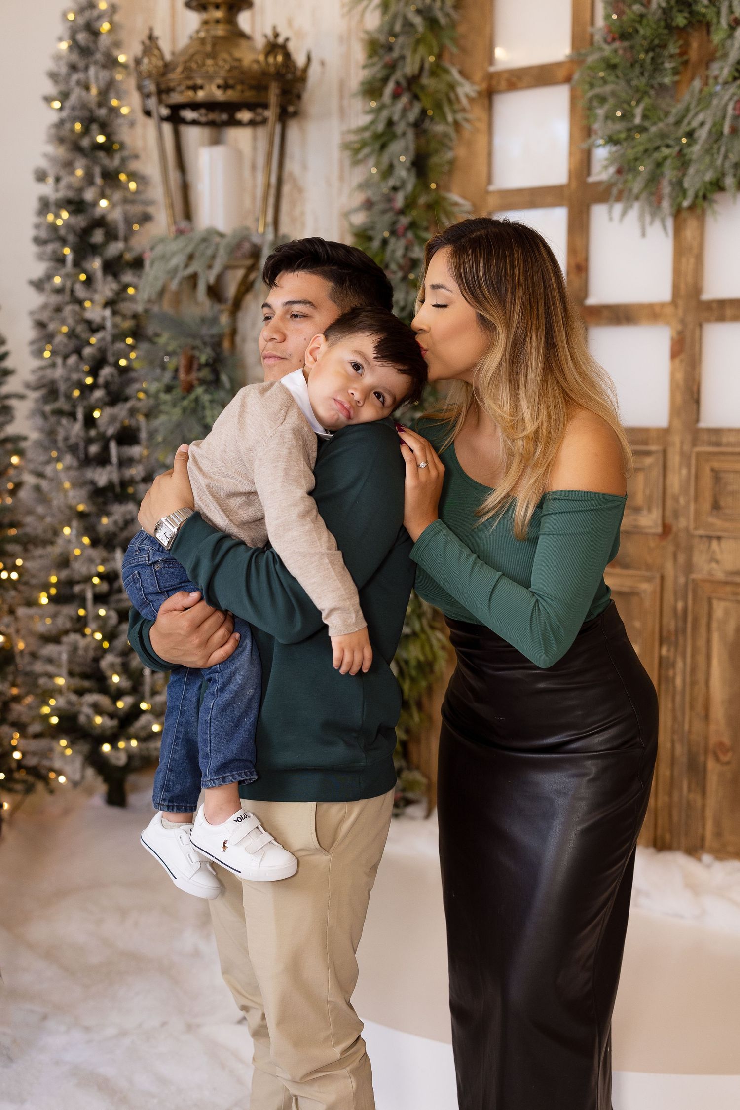 Family shares a loving moment in front of decorated Christmas tree with evergreen garland decor in festive holiday setting.
