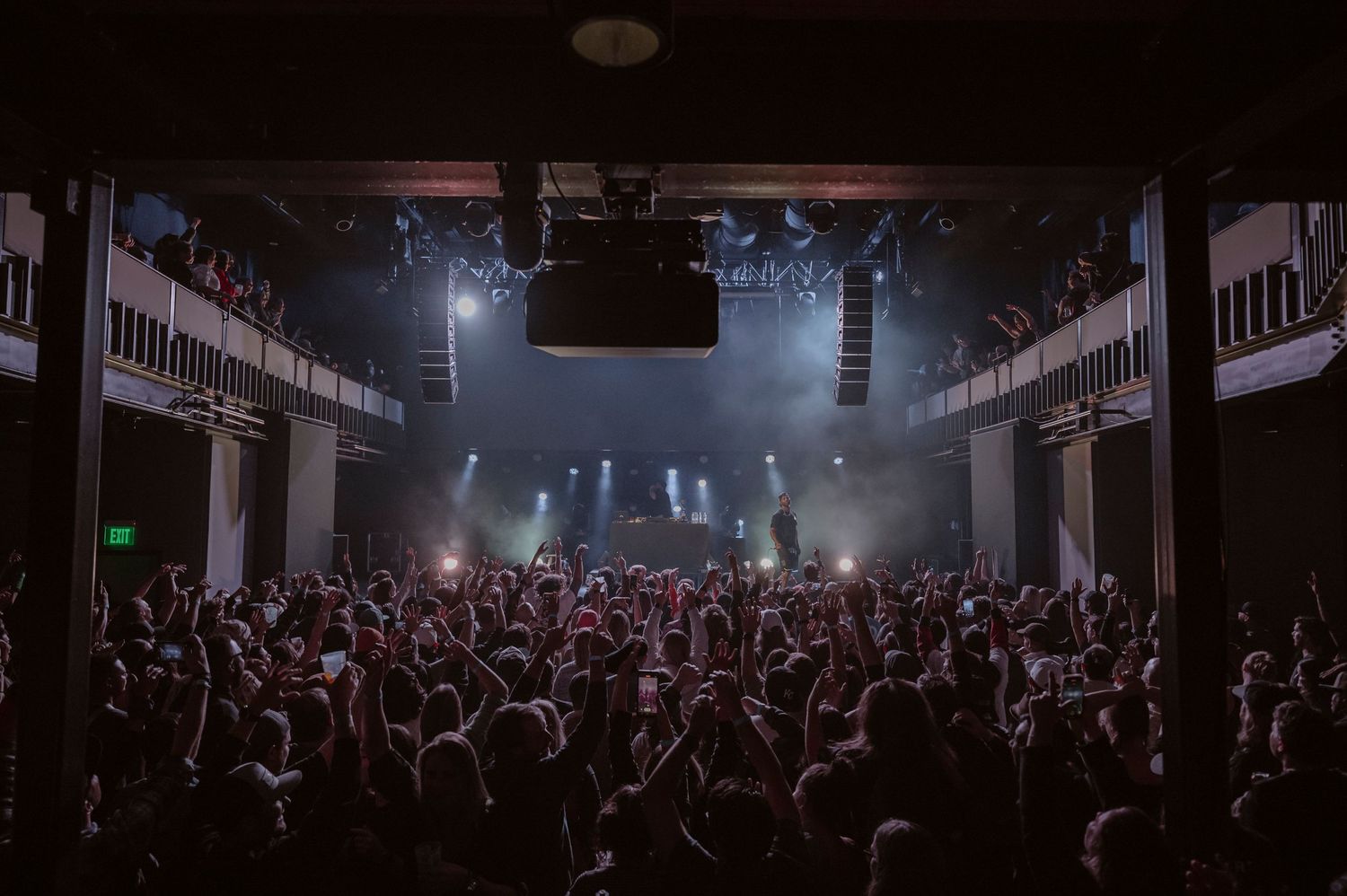 Crowded concert venue with dramatic lighting and fog effects creating an atmospheric ambiance.