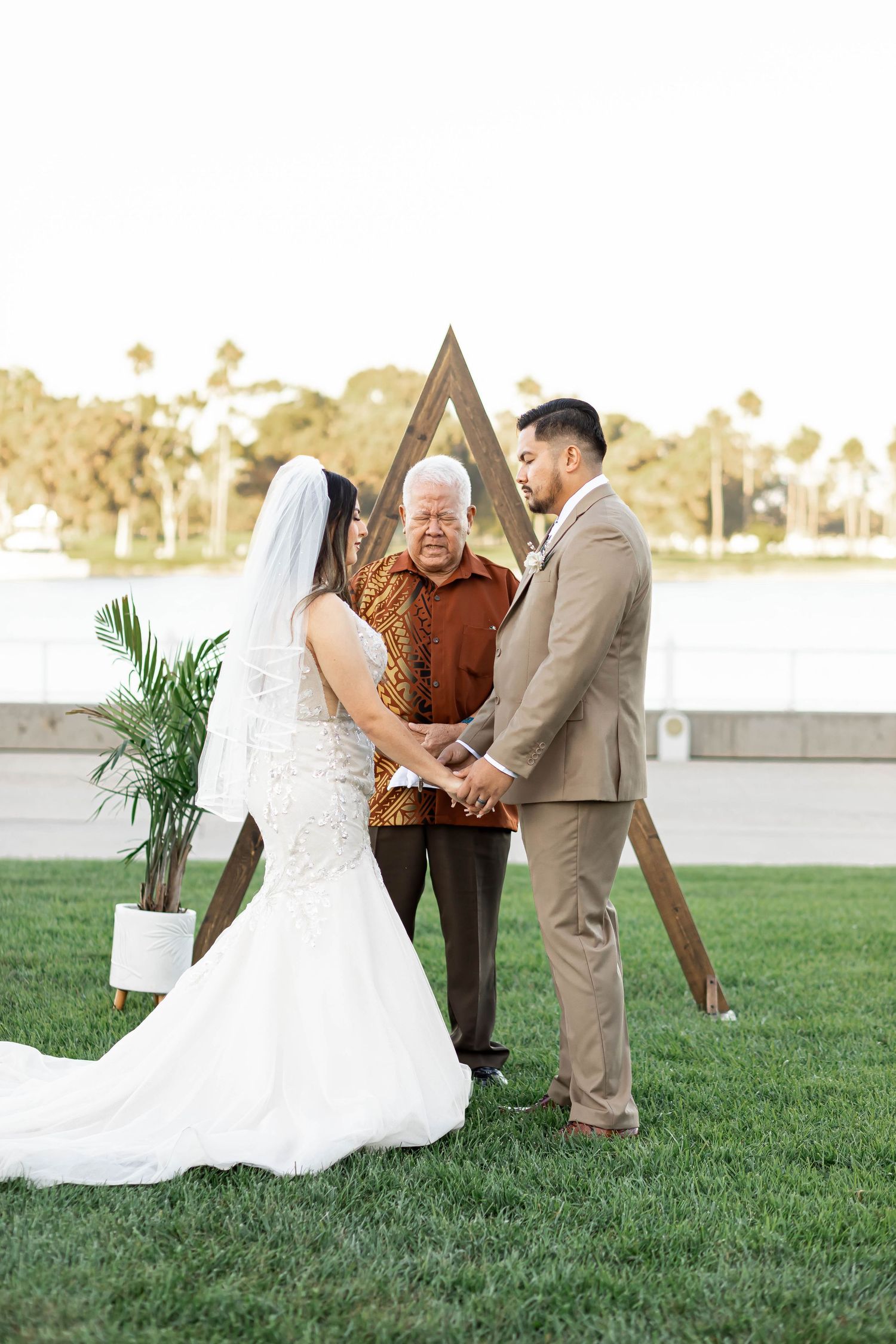 Outdoor wedding ceremony with wooden triangle arch and officiant.