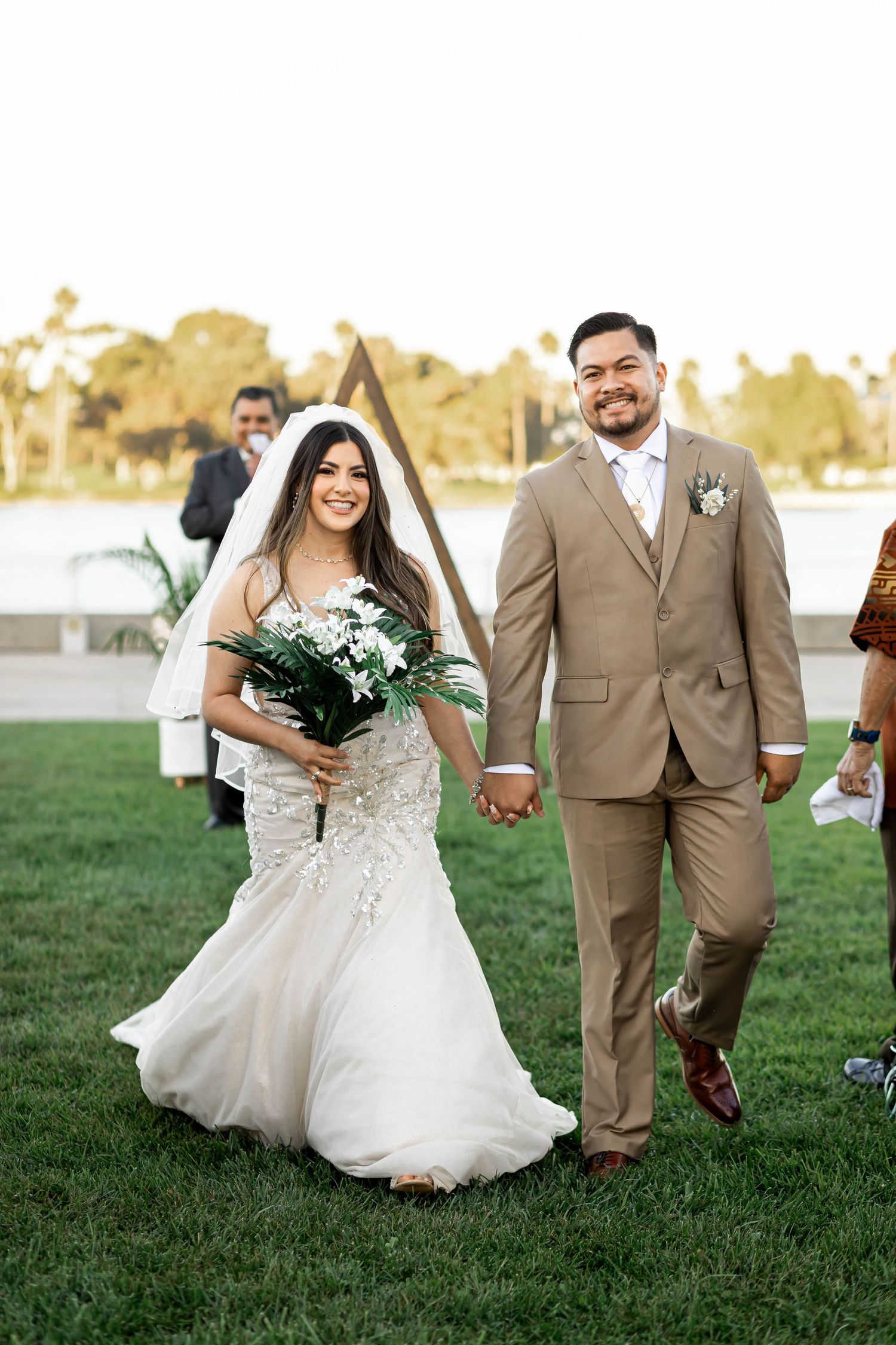 Newlyweds walking hand in hand on grass after ceremony.